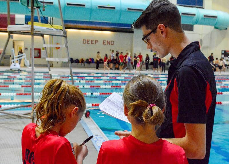 Coach speaks to two young participants on deck at a swimming pool